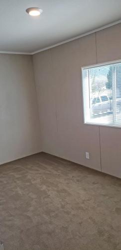 An empty room with tan carpet and a window.
